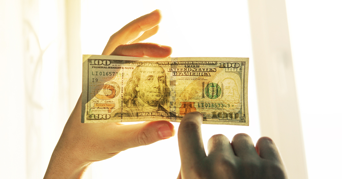 a 100 dollar bill where a person is looking at it through the light of a window to see if it is a forgery